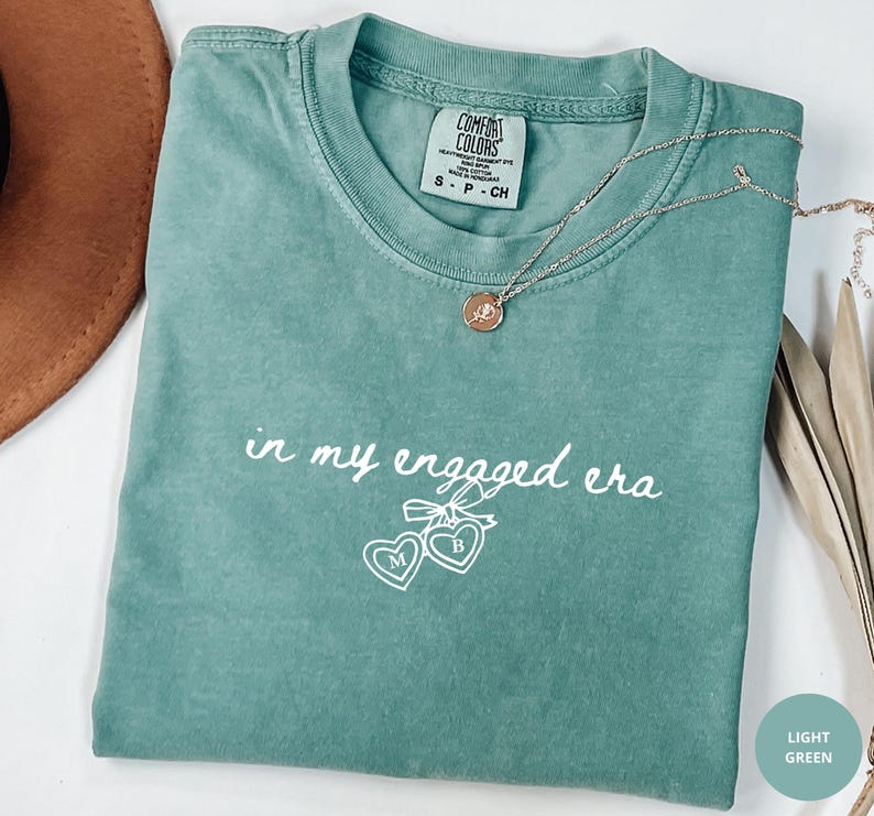 Light Green Comfort Colors® t-shirt with custom white text "in my engaged era" and heart lock graphic, perfect for brides-to-be and engagement gifts.