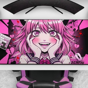 Puede incluir: Una alfombrilla de ratón Senpai rosa y negra con un personaje de estilo anime con pelo y ojos rosas. El diseño incluye corazones y la palabra "Senpai". También se ven un teclado, un ratón y un mando.