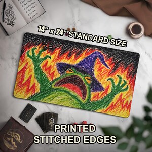 May include: A rectangular playmat featuring a crayon-style drawing of a green frog wearing a purple witch hat, surrounded by orange and yellow flames. The mat includes text stating 14" x 24" STANDARD SIZE and PRINTED STITCHED EDGES.
