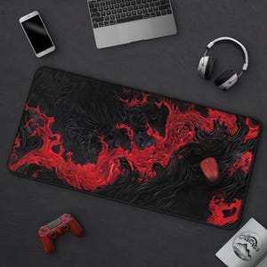 K&ouml;nnte beinhalten: Schwarzes und rotes Gaming-Mauspad mit einem wirbelnden, abstrakten Design. Das Pad hat eine strukturierte Oberfl&auml;che mit schwarzer Basis und leuchtend roten Akzenten. Eine rote Maus, ein Controller und weiteres technisches Zubeh&ouml;r sind sichtbar.