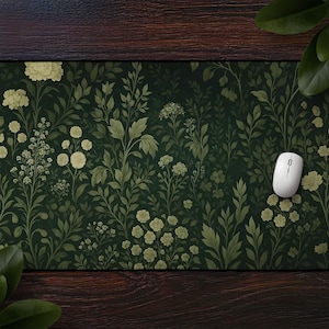 Könnte beinhalten: Rechteckiges Mauspad mit einem dunkelgrünen Blumenmuster mit cremefarbenen Blüten und Blättern. Eine weiße Computermaus liegt auf dem Pad. Das Design erinnert an eine botanische Illustration.