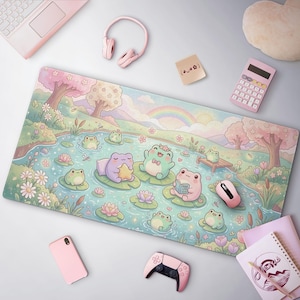 Puede incluir: Alfombrilla de ratón de color pastel con una escena de estanque ilustrada con ranas de dibujos animados sobre nenúfares. El diseño incluye un arcoíris, flores y árboles. Un ratón rosa, auriculares y otros accesorios rodean la alfombrilla.