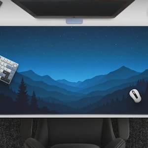 May include: A large rectangular desk mat featuring a mountain landscape design in shades of blue. A white keyboard and mouse are positioned on the mat, with a computer monitor and coffee cup in the background. The mat's design includes a starry night sky.