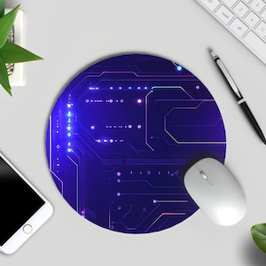 Peut inclure: Tapis de souris rond bleu et violet avec un motif de circuit imprim&eacute;. Une souris d'ordinateur blanche repose sur le tapis. Un clavier blanc, un stylo et un smartphone sont &eacute;galement visibles, ainsi qu'une petite plante en pot.