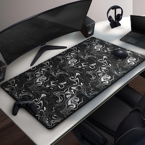 May include: A large rectangular black and white marbled pattern mouse pad. The pad is on a white desk with a computer monitor, speakers, a laptop, a mouse, a controller, and headphones.