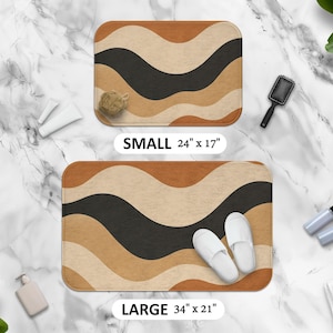 May include: Two rectangular bath mats with a wavy pattern in shades of brown, tan, and black. The smaller mat is 24 inches by 17 inches, and the larger mat is 34 inches by 21 inches. The mats are displayed with bathroom accessories.