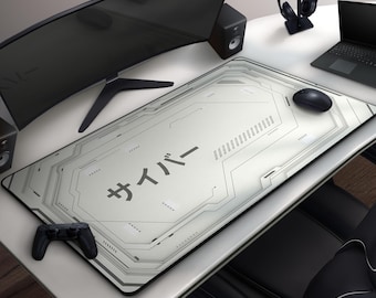 May include: A white and gray rectangular gaming mousepad with a circuit board design and Japanese text. A black mouse, controller, and other electronics are on a white desk. The mousepad measures approximately 36 inches long.