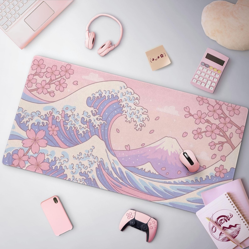 K&ouml;nnte beinhalten: Ein pastellrosa Schreibtischunterlage mit einem japanischen Wellenmuster, Kirschbl&uuml;ten und dem Berg Fuji. Die Unterlage ist von rosa Zubeh&ouml;r umgeben, darunter eine Maus, Kopfh&ouml;rer und ein Taschenrechner. Ein Laptop und ein Gamecontroller sind ebenfalls zu sehen.