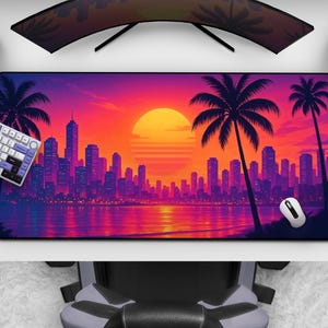 Può includere: Un tappetino per mouse rettangolare con un vivace tramonto su uno skyline cittadino con palme. La tavolozza dei colori comprende sfumature di arancione, viola e rosa. Sono visibili un mouse, una tastiera e un controller di gioco bianchi.