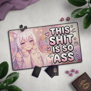 May include: A rectangular desk mat featuring an anime-style character with long white hair and cat ears, wearing a beige sweater. The text "THIS SHIT IS SO ASS" is printed in large, bold, pink-outlined letters alongside small heart and star icons.