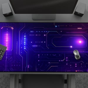 Peut inclure: Tapis de souris rectangulaire avec un motif de circuit imprim&eacute; dans des tons violets et bleus. Un clavier et une souris noirs sont pos&eacute;s dessus. Le tapis est sur un bureau gris avec un &eacute;cran d'ordinateur et des haut-parleurs.