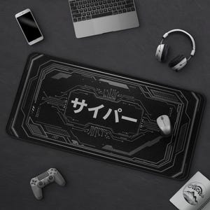 May include: Black rectangular gaming mouse mat with a circuit board design and Japanese text. A laptop, headphones, a mouse, a smartphone, and a game controller surround the mat.