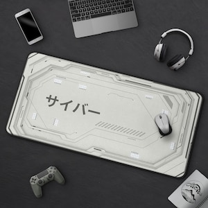 Peut inclure: Un grand tapis de souris rectangulaire blanc et gris avec le mot japonais "サイバー" imprimé dessus. Le tapis de souris a un design futuriste de circuit imprimé. Une souris sans fil, un casque et une manette de jeu sont également visibles.