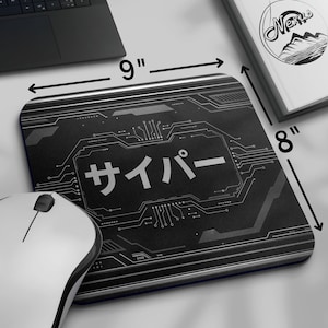 May include: Black rectangular mousepad, 23 cm by 20 cm, featuring a circuit board design and Japanese text. A white mouse and a laptop are visible. A book with a mountain logo is also present.