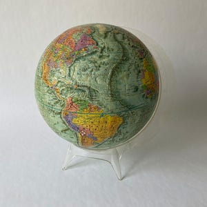 May include: A vintage globe with a green and yellow map on a clear plastic stand.