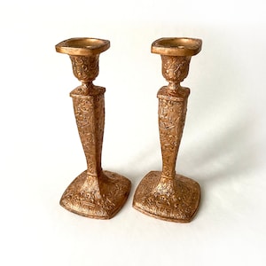 Puede incluir: Dos candelabros de metal dorado con un diseño ornamentado. Los candelabros están sobre un fondo blanco.