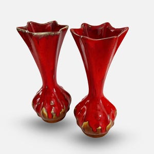 Puede incluir: Dos jarrones de cerámica roja con una forma única. Los jarrones tienen una base bulbosa con un diseño texturizado y una parte superior acampanada en forma de estrella. Los bordes tienen un ribete dorado. Estos jarrones decorativos son ideales para la decoración del hogar.