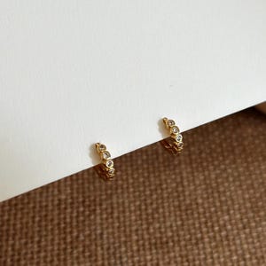 May include: A pair of gold hoop earrings with small clear cubic zirconia stones set in the metal. The earrings are simple and elegant.