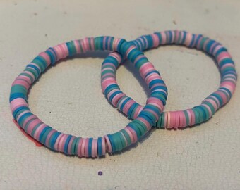 May include: Two bracelets made of colorful, stacked, round beads. The beads are pink, blue, and green.