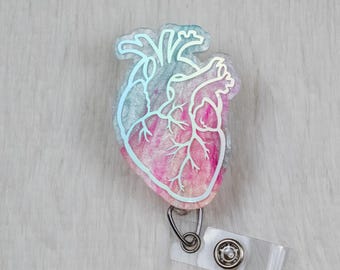 May include: A pink and blue iridescent heart-shaped badge holder with a clear plastic clip and a silver swivel clasp.