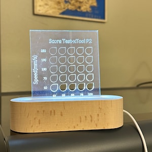 May include: A clear acrylic sheet with a grid of circles and the text "Score Test-xTool P2" and "Speed (mm/s)". The sheet is illuminated from below with a white light.