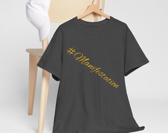 Op de afbeelding: Een donkergrijs T-shirt met een gouden hashtag en het woord "Manifestation" in cursief.