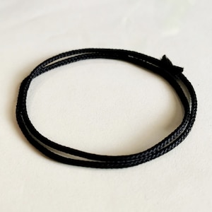Peut inclure: Un cordon noir, d'environ 45 cm de long, est enroulé en cercle. Le cordon est fait d'un matériau souple et flexible, idéal pour l'artisanat ou la fabrication de bijoux.