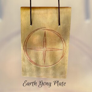 以下が含まれることがあります： 長方形の金色のEarth Gong Plate。円の中に十字の模様があります。プレートは2本の濃い茶色のコードで吊り下げられています。「Earth Gong Plate」の文字がプレートの下部に筆記体で書かれています。
