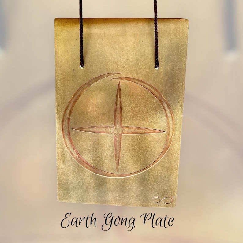 以下が含まれることがあります： 長方形の金色のEarth Gong Plate。円の中に十字の模様があります。プレートは2本の濃い茶色のコードで吊り下げられています。「Earth Gong Plate」の文字がプレートの下部に筆記体で書かれています。