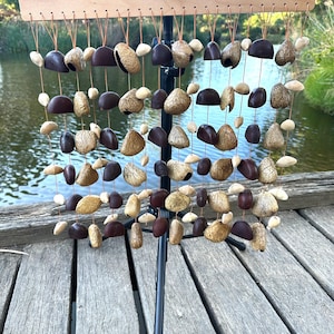 May include: A wooden frame with a series of strings hanging from it. Each string has a variety of brown and beige seed pods attached to it. The frame is mounted on a black tripod stand. The frame has the word "LUNE" printed on it.