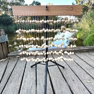 May include: A wooden frame with a series of seashells hanging from it. The frame is mounted on a black tripod stand. The seashells are arranged in rows and are strung together with twine. The frame has the word "Infinity" written on it.