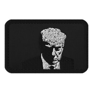 Op de afbeelding: Zwart-witte geborduurde patch met een portret van een man met een serieuze uitdrukking. De patch is rechthoekig en heeft een zwarte achtergrond.