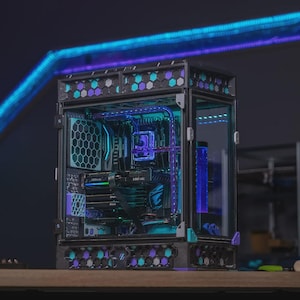 May include: A custom PC case with a transparent side, displaying internal components. The black frame has teal and purple hexagonal accents. The interior is lit with blue and purple LEDs, creating a vibrant display. The case sits on a wooden surface.