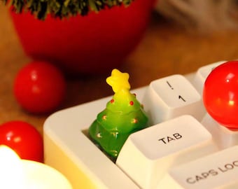 Könnte beinhalten: Ein festliches Weihnachtsbild mit einer Miniatur-Weihnachtsbaumdekoration mit gelbem Stern auf einer weißen Tastatur. Rote Kugeln und eine rote Schale mit einem grünen Kranz sind ebenfalls zu sehen, was eine festliche Atmosphäre schafft.