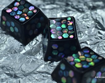 Könnte beinhalten: Drei schwarze Keycaps mit schillernden sechseckigen Mustern. Die Keycaps bestehen aus schwarzem Harz mit glänzender Oberfläche. Die sechseckigen Muster bestehen aus einem schillernden Material, das in verschiedenen Farben schimmert.