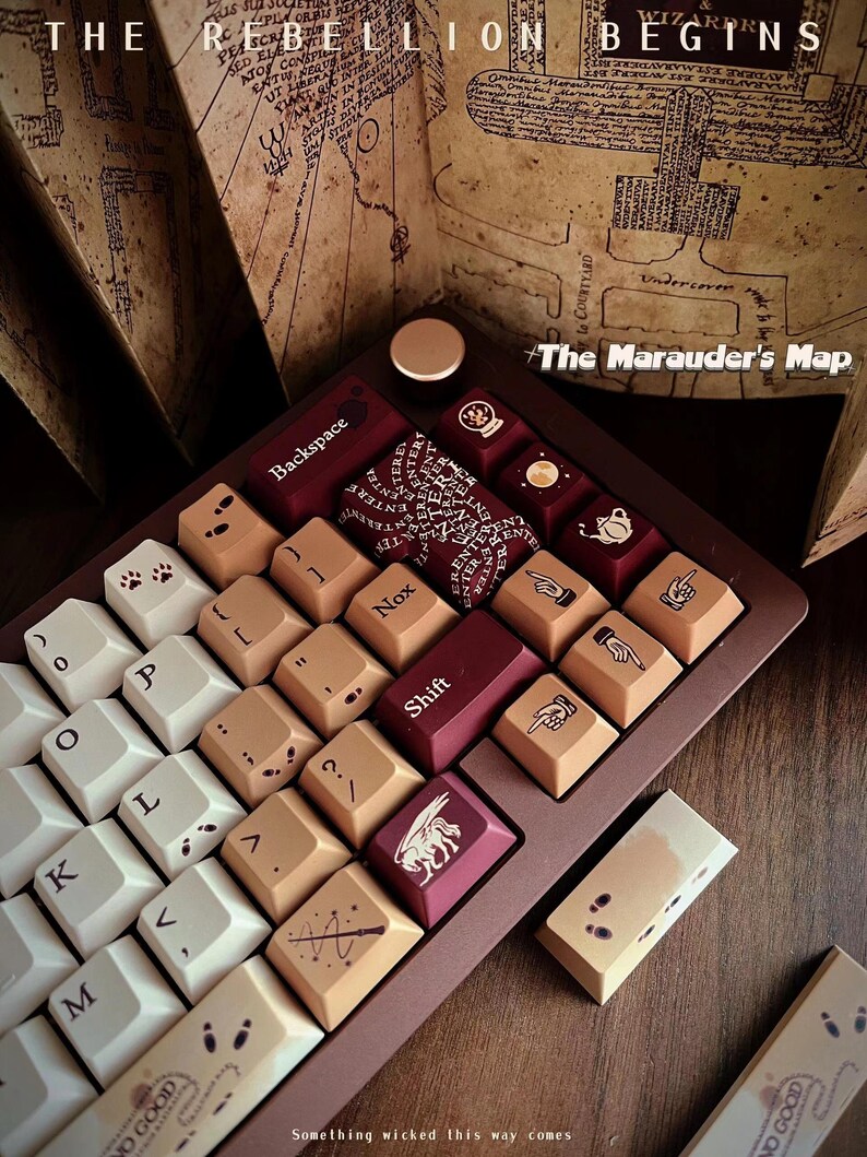 May include: A custom keyboard with keycaps featuring icons and text, including "Backspace" and "Shift." The keyboard has a brown frame and a variety of keycap colors, with the text "The Marauder's Map" and "Something wicked this way comes."