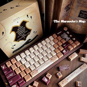May include: A custom mechanical keyboard with keycaps in cream, brown, and burgundy. The keyboard has a dark brown frame and features text and graphics, including "The Marauder's Map" and "I Solemnly Swear That I Am Up To No Good." The box reads "The Marauder's Map".