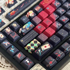 May include: A custom mechanical keyboard with a black frame and a variety of keycaps. The keycaps feature intricate designs in red, blue, and gold, with some displaying illustrations and text. The keyboard's design is artistic and detailed.