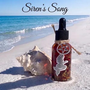 May include: A clear glass dropper bottle filled with amber liquid and botanical elements, featuring a silver mermaid silhouette sticker, a silver pentagram charm tied with twine around the black cap, and the text Siren's Song above it.