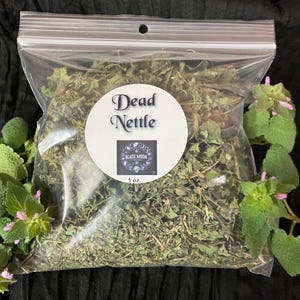 May include: A clear plastic bag filled with dried Dead Nettle herbs. A white circular label displays the text "Dead Nettle" and a small logo. The bag contains 1 oz. of herbs and is surrounded by green leaves with pink flowers.