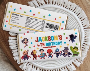 May include: Two candy bar wrappers with a superhero theme. One wrapper has a nutrition facts label. The other wrapper says "Jackson's 4th Birthday" with superhero illustrations and the text "Thanks for coming!" The wrappers are decorated with colorful stars.