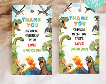 Puede incluir: Etiquetas de regalo con temática de dinosaurios con el texto "THANK YOU FOR MAKING MY BIRTHAY SPECIAL LOVE JACKSON". Las etiquetas presentan ilustraciones de varios dinosaurios, volcanes y plantas tropicales. Las etiquetas están ensartadas con hilo blanco.