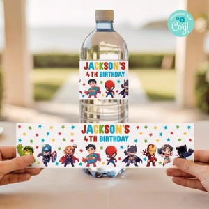 Könnte beinhalten: Eine Wasserflasche mit einem individuellen Etikett mit dem Text "JACKSON'S 4TH BIRTHDAY" und Superhelden-Illustrationen. Das Etikett ist um die Flasche gewickelt, und ein passendes Etikett wird darunter gehalten. Der Hintergrund ist unscharf.