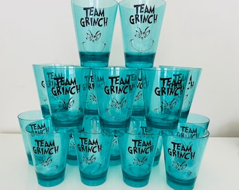 May include: A stack of ten turquoise blue plastic cups with a black and white graphic of the Grinch's face and the text "Team Grinch" on each cup.