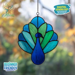 Pode incluir: Um apanhador de sol de vitral em forma de pavão, em tons de azul e verde, pendurado por uma corrente. O design do pavão apresenta uma cauda em forma de leque e um corpo detalhado. O texto "Beginner Friendly" é visível.