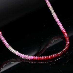 Può includere: Una collana di pietre preziose graduate con perline rosa, rosse e bianche. La collana è realizzata con piccole perline rotonde che sono infilate su un filo sottile.