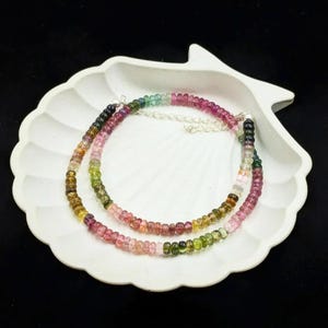 May include: A multi-colored gemstone necklace with pink, green, and black beads. The necklace is made of round beads and is strung on a silver chain.