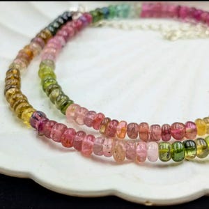 May include: A double strand necklace made of small, round, multi-colored gemstones. The necklace features a gradient of colors, starting with green and yellow, transitioning to pink and red.