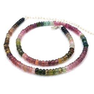 May include: A multi-colored gemstone necklace with a silver chain. The necklace is made of round beads in shades of pink, green, blue, and black.
