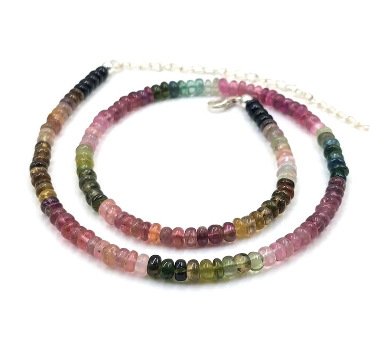 May include: A multi-colored gemstone necklace with a silver chain. The necklace is made of round beads in shades of pink, green, blue, and black.